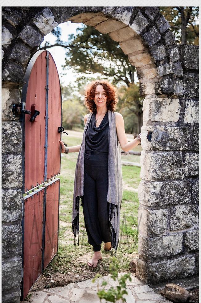 Portrait of the practitioner standing at an open garden gate under a stone archway