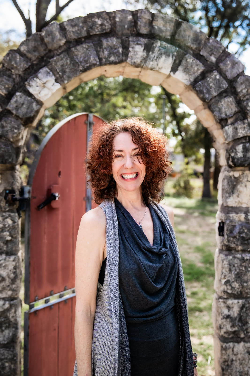 Maria laughing beneath a limestone archway, a red wooden door behind her