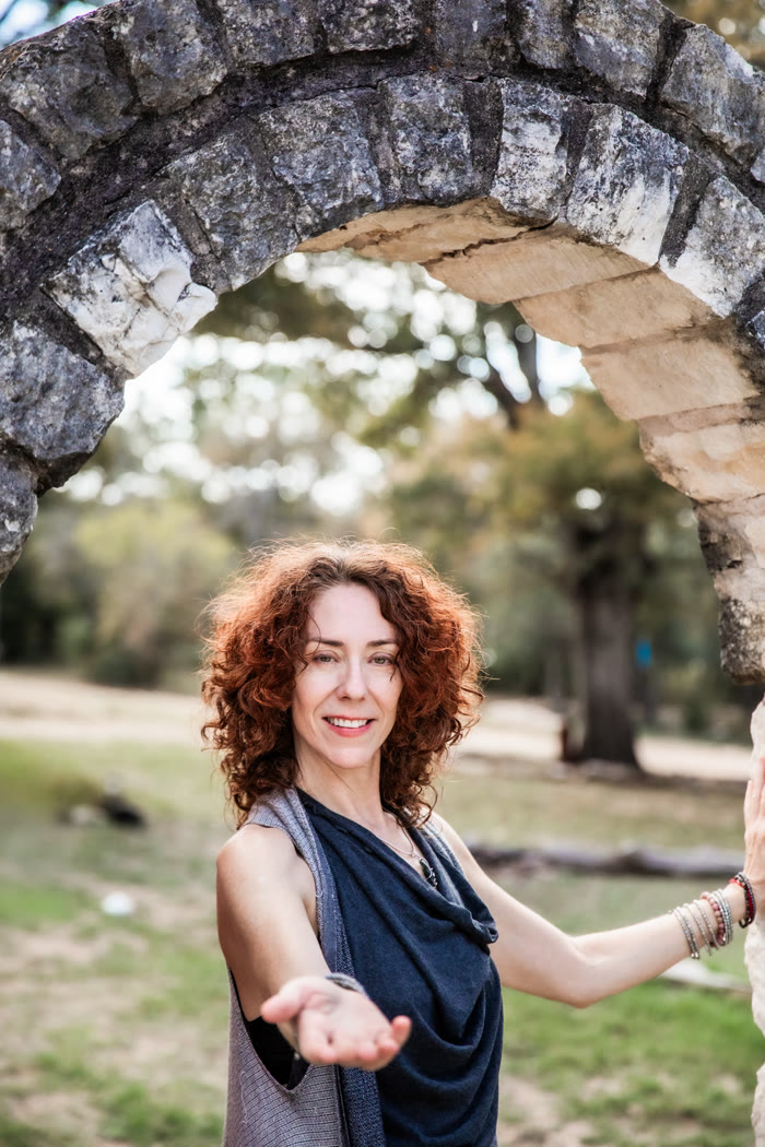 Maria under a wide stone arch, reaching one open hand toward you