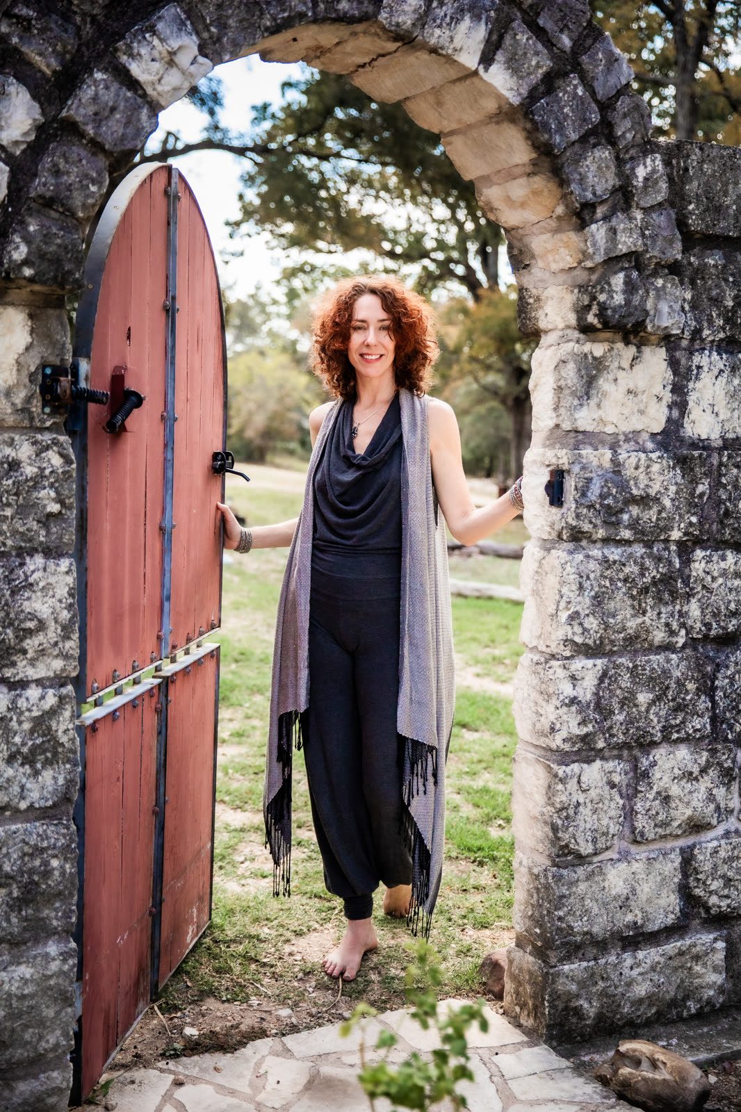 Maria standing barefoot in an open red door inside a stone archway, smiling